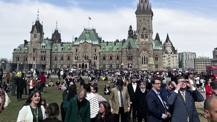 Des centaines de personnes sont sur la pelouse de la colline du Parlement dont certaines portent des lunettes pour observer l'éclipse du 8 avril. 