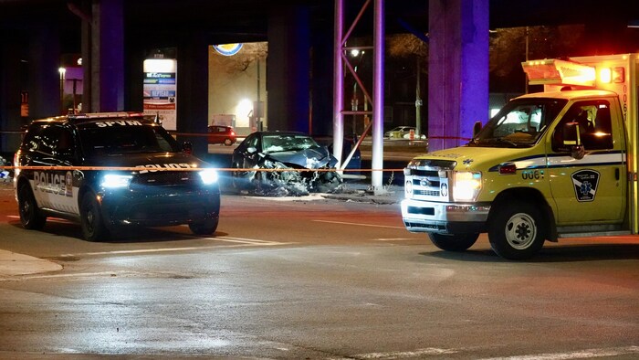 Une voiture de police et une ambulance stationnées dans un périmètre de sécurité.