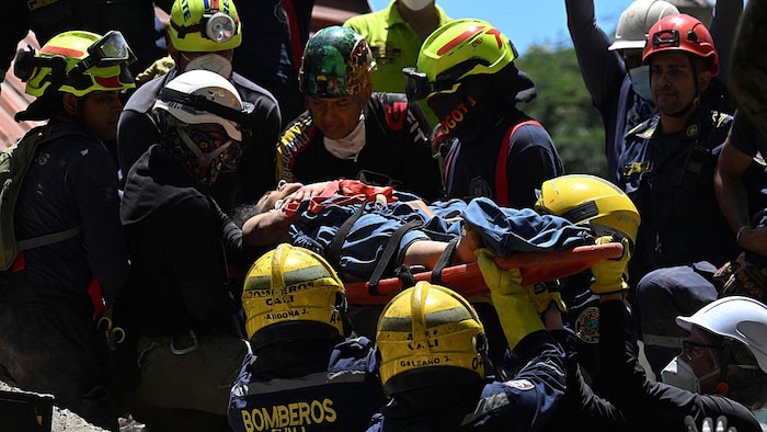 Des pompiers et des secouristes évacuent une personne des décombres d’un immeuble effondré.