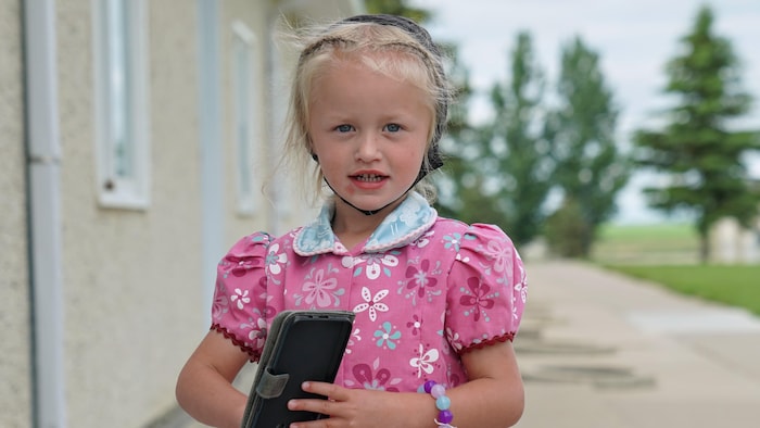 Une petite fille huttérite de la colonie de White Lake, en Alberta, tient un téléphone dans ses mains le 6 juillet 2022. 