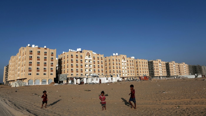 Des enfants jouent sur un terrain de sable devant des blocs d'immeubles.