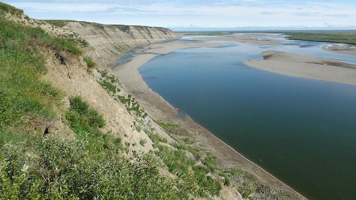 Un cours d'eau s'étend à perte de vue avec des falaises ensablées l'entourant à sa gauche.