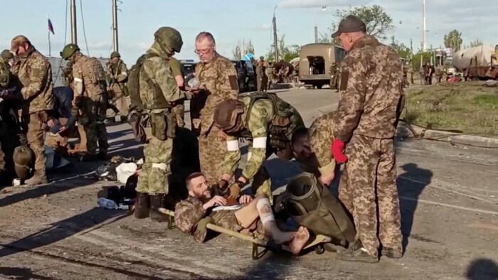 Des militaires sont penchés sur un autre militaire blessé à la jambe, couché dans une civière posée sur le sol.