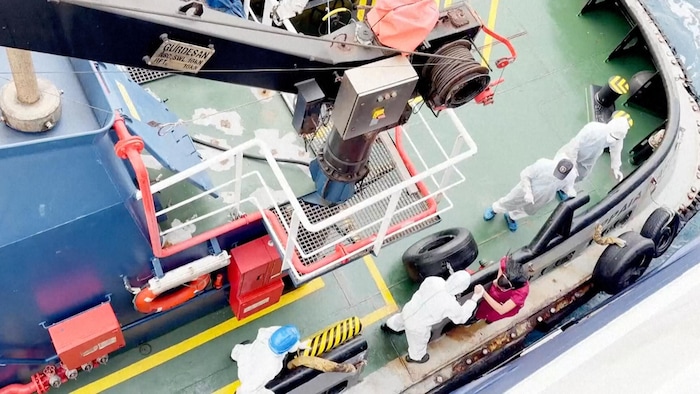 Des gens portant des combinaisons blanches montent sur le pont d'un bateau.