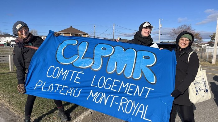Marie-Ève d'Entremont et ses deux collègues tiennent une grande banderole. 