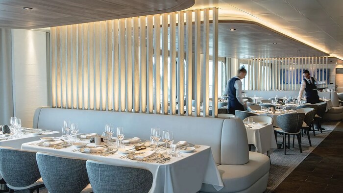 Un restaurant dans le navire Commandant Charcot, avec des tables dressées et deux sevreurs.