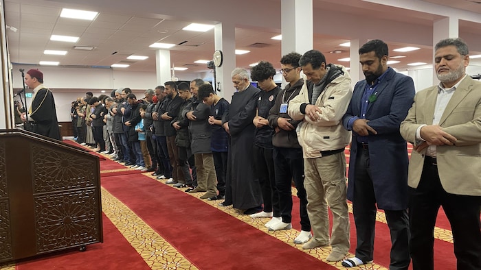رجال واقفون في قاعة مسجد ويؤدون الصلاة.