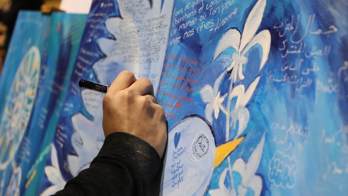 Une personne écrit un mot dans une œuvre collective lors de la soirée de commémoration du 2e anniversaire de l'attentat à la Grande mosquée de Québec
