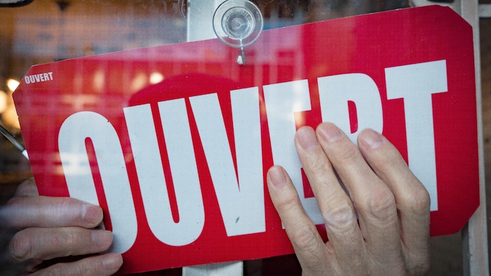 Des mains tournent une pancarte pour indiquer que le magasin est ouvert.