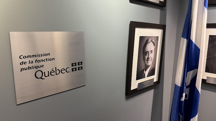 Commission de la fonction publique. La plaque est placée au milieu de photographies encadrées d’anciens présidents de la Commission et près d’un drapeau du Québec.
