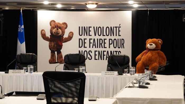 Un ourson en peluche à côté d'une affiche de la commission Laurent