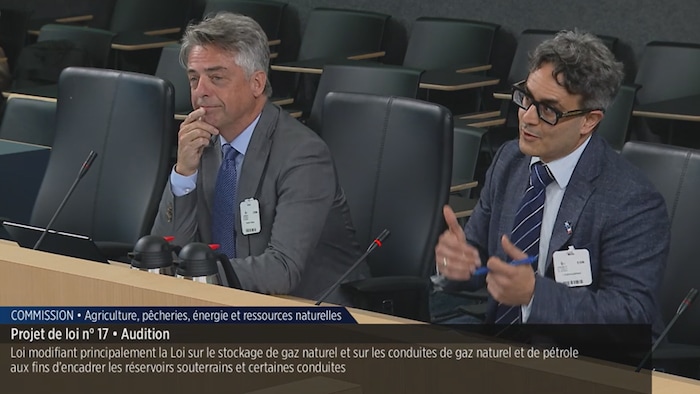 Les deux hommes sont assis autour d'une table et s'expriment.