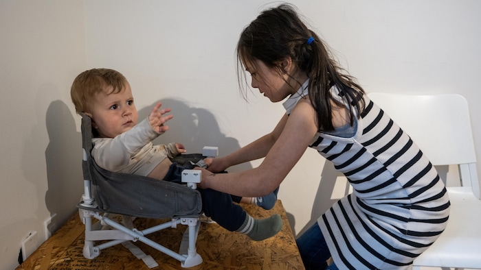 Une jeune fille installe un bébé dans une chaise.