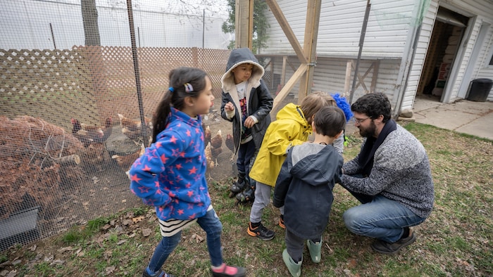 Un homme et des enfants près d'un enclos avec des poules.