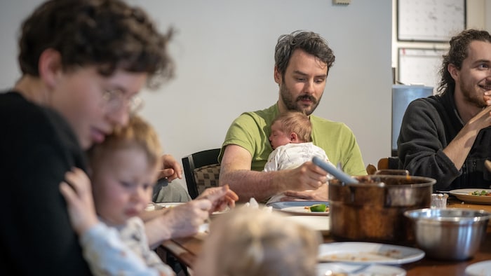 Un homme avec un bébé naissant dans les bras est attablé avec d'autres personnes.