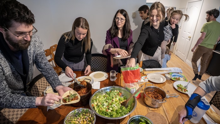 Des adultes entourent une table garnie de différents plats.