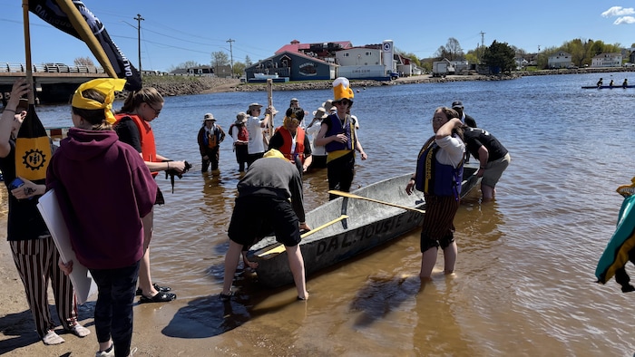 Cinq étudiants les pieds dans l'eau maintiennent leur canoë près de la berge.