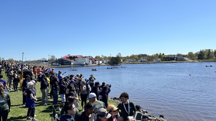 Une foule sur une berge regarde des canoës en béton sur la rivière.