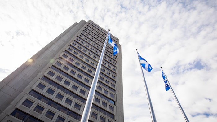 Un gratte-ciel en béton devant lequel se trouve trois drapeaux du Québec.