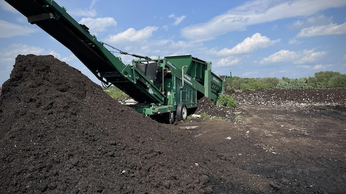 Un camion tamise une montagne de compost.