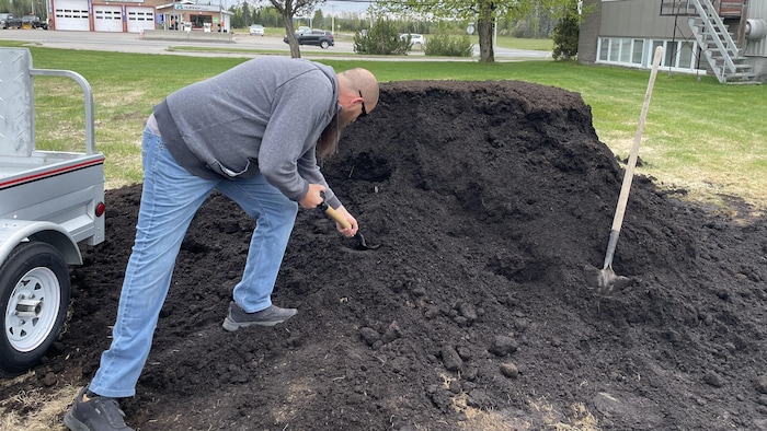 Un homme plonge un pelle dans un amas de compost