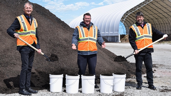 Trois hommes soulevant les pelles remplies de compost.