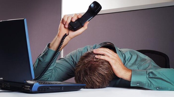 Un homme pose sa tête sur son bureau, le téléphone à la main.