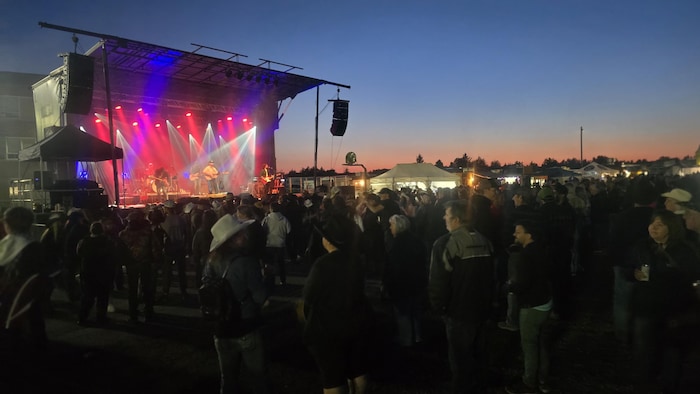 Des dizaines de personnes assistent à un concert à la tombée de la nuit.