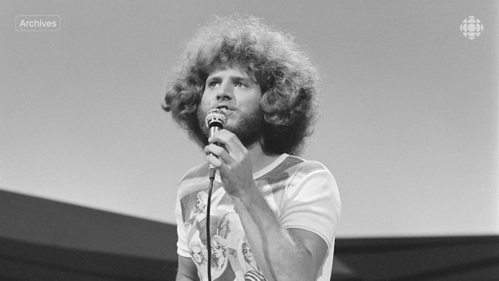 Un homme aux cheveux frisés chante en tenant un micro dans sa main.