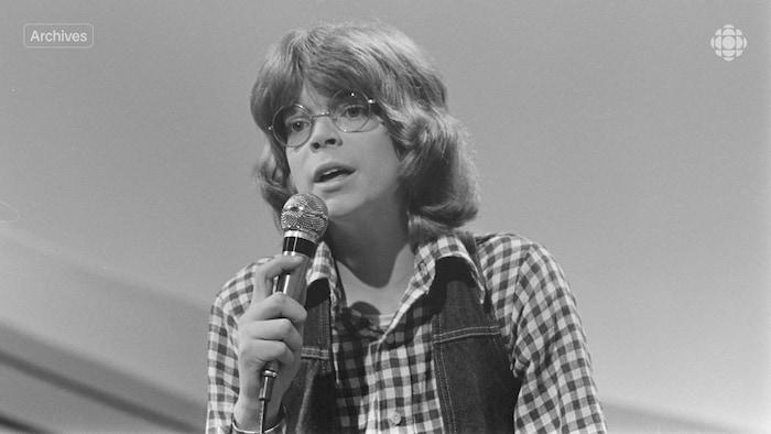 Un jeune garçon portant des lunettes rondes chante une chanson en tenant un micro dans sa main.