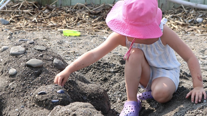 Un enfant dépose un caillou sur une structure de sable. 