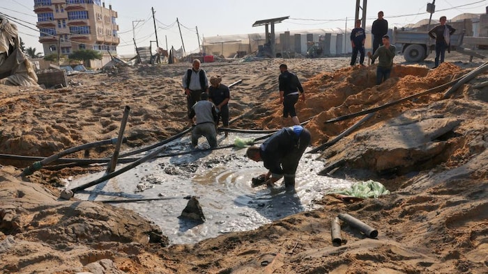 Des travailleurs palestiniens s'affairent à réparer une conduite d'eau endommagée au milieu d'une route de sable.