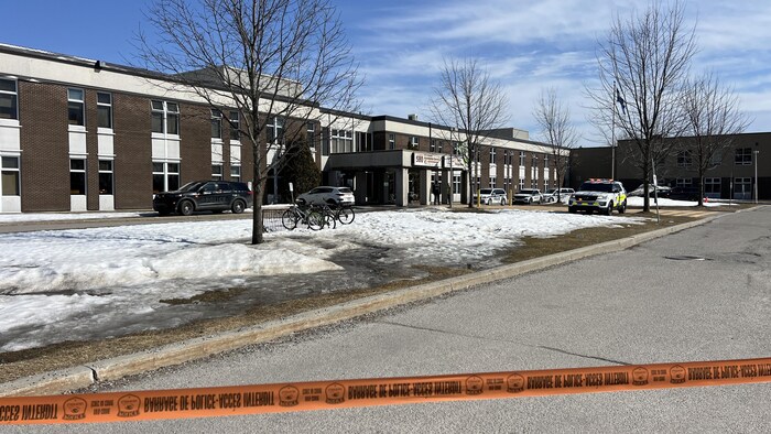 Un ruban policier devant une école derrière des véhicules de police.