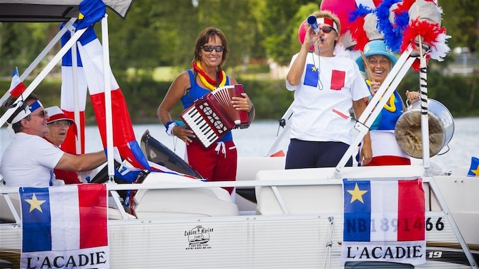Sur un bateau, plusieurs personnes font la fête, habillées aux couleurs de l'Acadie.