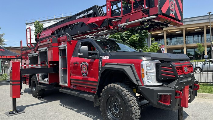 Sur la photo se trouve un énorme véhicule utilitaire léger. Il est doté d'une grue sur le dessus. Le véhicule en question est neuf et tapissé de logos des services incendies.