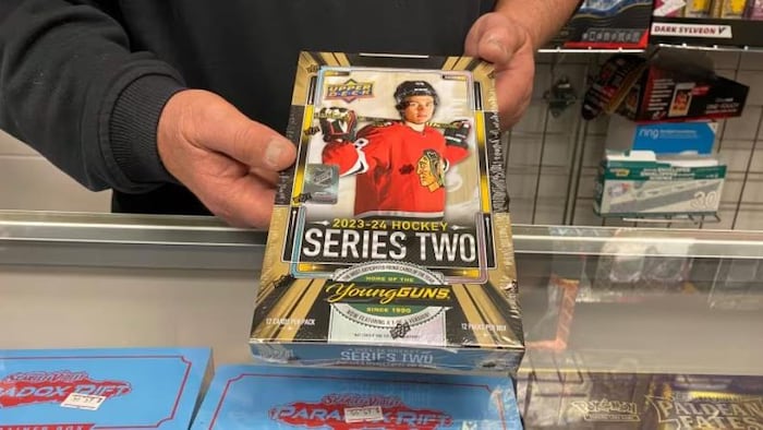 Le copropriétaire du magasin de cartes de collection The Nutman Cards and Collectibles à Regina, Tanner Piper, tient une boîte contenant des paquets d'un nouveau jeu de cartes de hockey, qui contient la carte de recrue Young Guns de Connor Bedard.