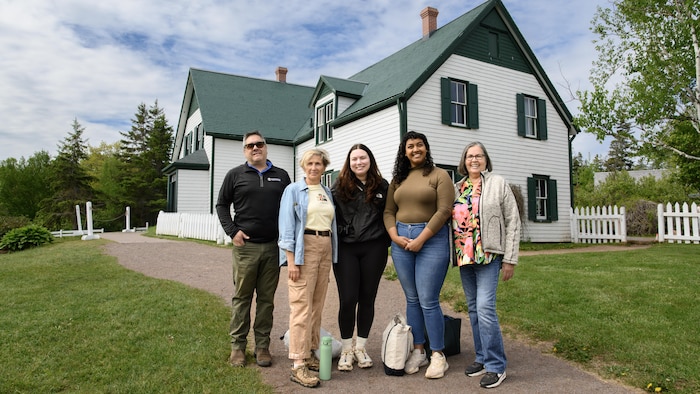 Groupe de cinq personnes photographiées dehors devant une maison aux pignons verts.