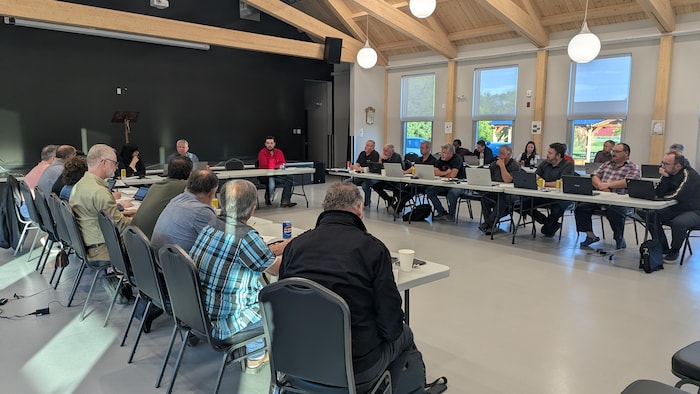 Des maires et mairesses, en plus du préfet et de la directrice générale, sont assis autour de tables collées dans un centre communautaire.