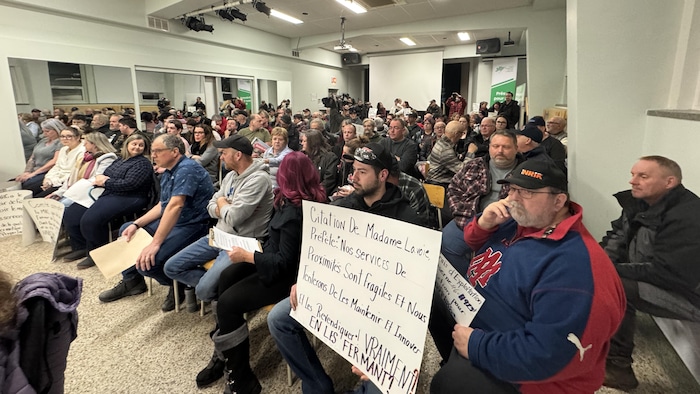 Des gens assis dans une salle. Certains tiennent des affiches et des pancartes.