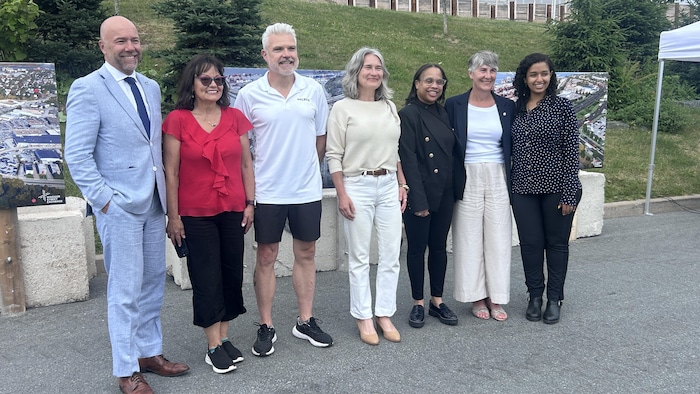 Photo de groupe de sept personnes dans un stationnement, avec une petite colline gazonnée plantée de sapins juste derrière.