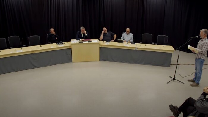 Un homme se tient devant un panel d'élus