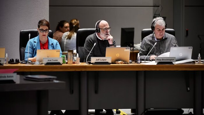 Les conseillers municipaux d'Ottawa Ariel Troster, Jeff Leiper et Riley Brockington sont assis derrière un bureau pendant une séance du conseil municipal.
