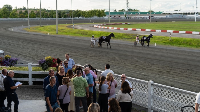 Plusieurs personnes parlent devant des courses de chevaux.