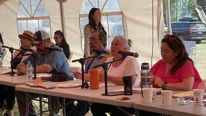 Cinq personnes assises à une table, chacune devant un microphone.