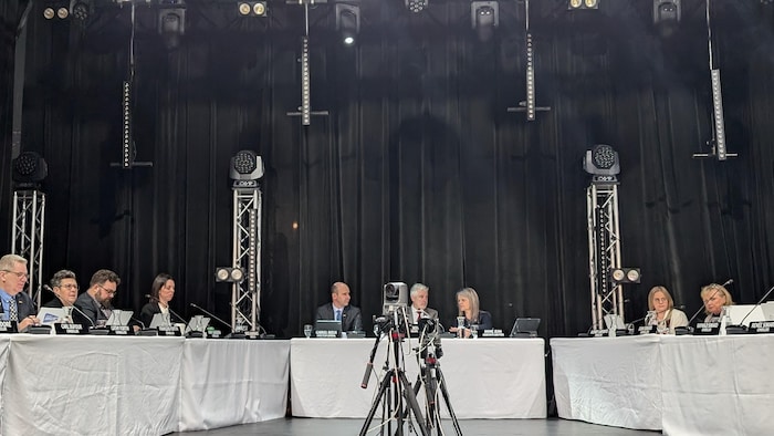 Les conseillers sont assis derrière une table blanche dans une salle noire.