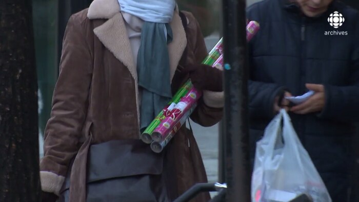 Une femme anonyme, en manteau d'hiver, tient des rouleaux de papier d’emballage.
