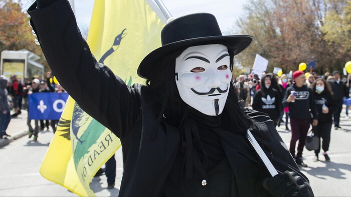 Un homme portant un masque anonyme lève le bras en signe de victoire alors qu'il manifeste dans la rue. 