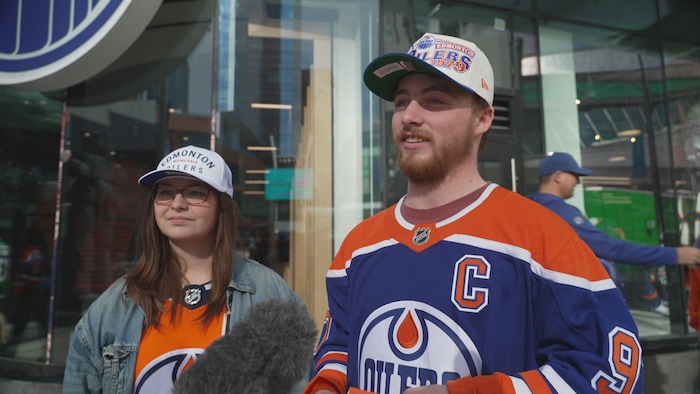 Deux personnes sont debout dehors devant un magasin des Oilers d'Edmonton. 