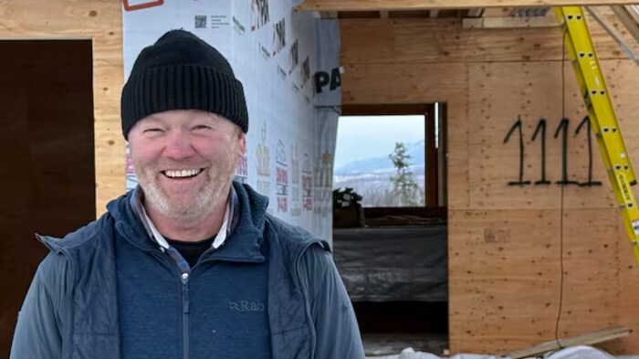 Un homme sourit devant une maison en construction.