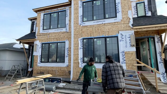 Deux personnes avec des outils devant une maison en construction.